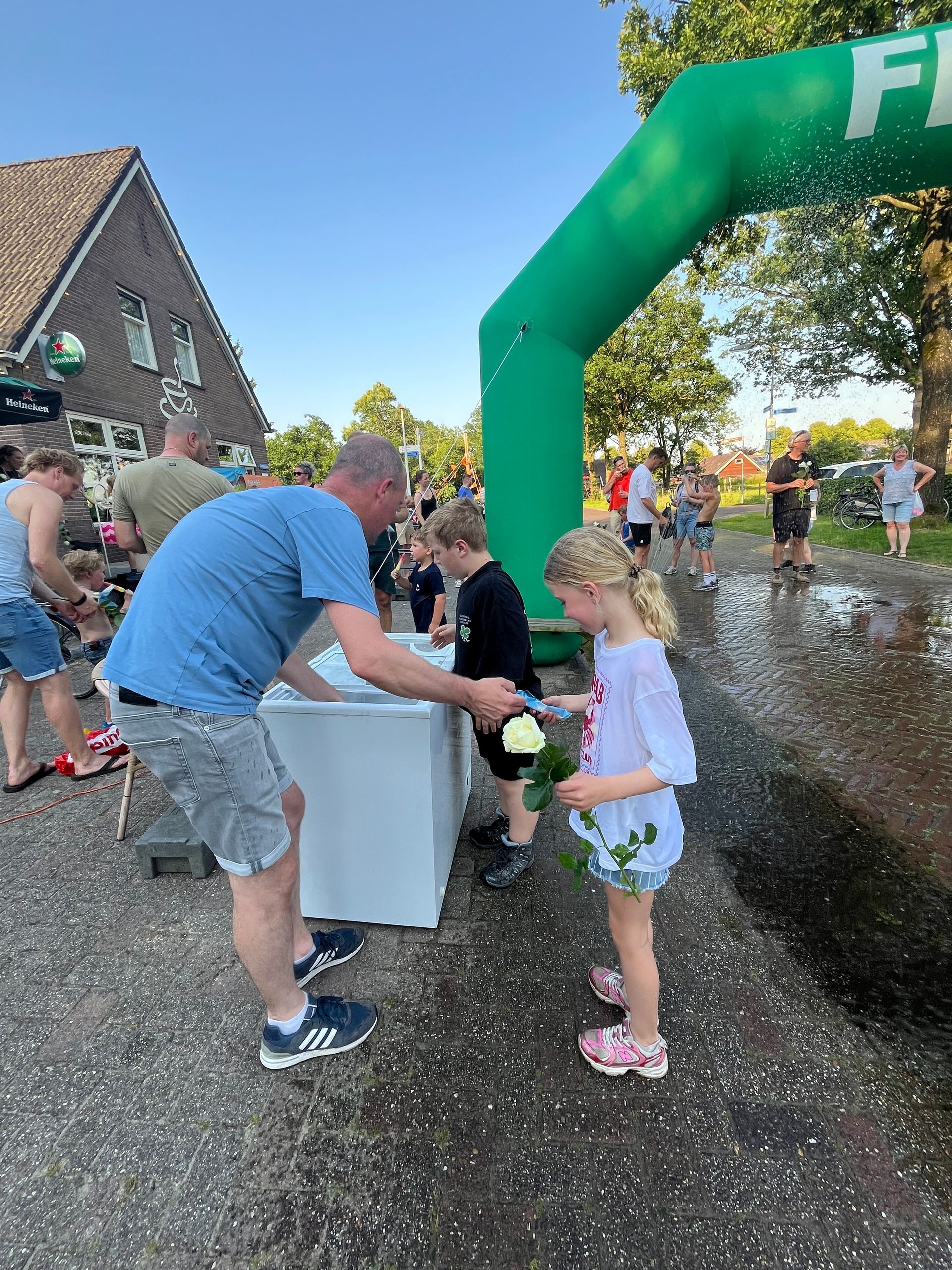 Kinderen geven waterballonnen aan elkaar door onder een groene opblaasbare boog tijdens een evenement in de buitenlucht.