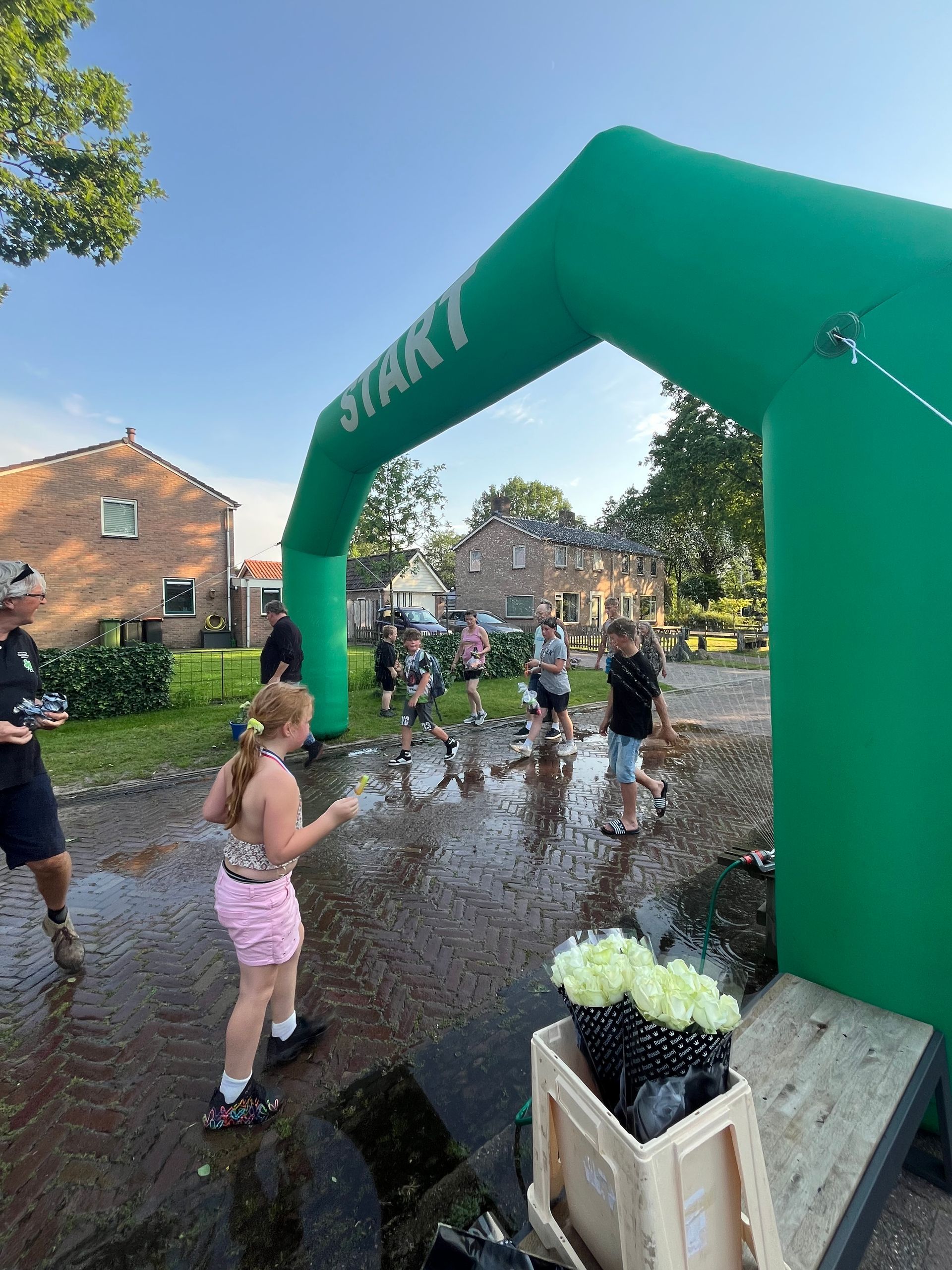 Mensen rennen door een natte, opblaasbare startboog bij de finish van een liefdadigheidsloop in de openlucht.