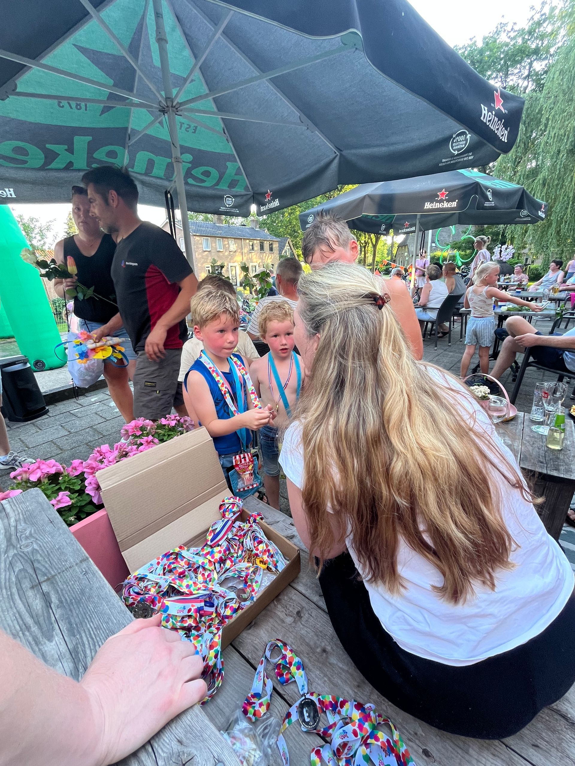 Mensen zitten onder parasols op een openluchtmarkt, met een doos kleurrijke snoepjes op de voorgrond.