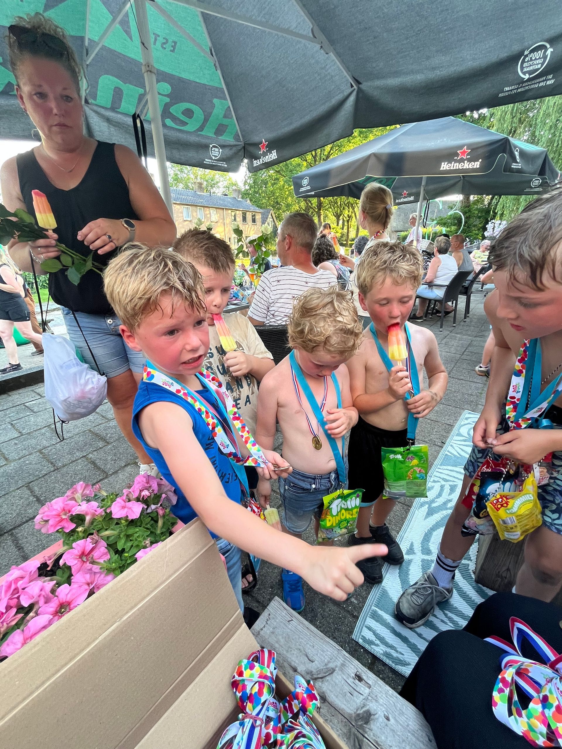Kinderen die snoepjes aannemen van moeder op een buitenevenement met roze bloemen en parasols.