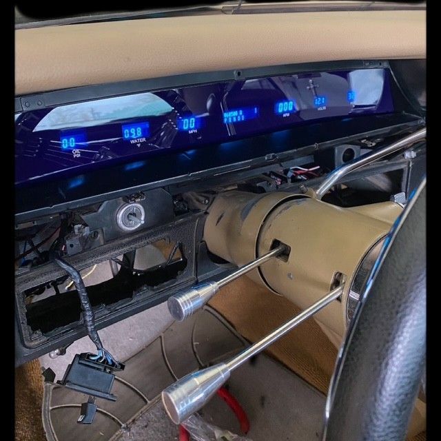 Dashboard of a classic car with blue digital gauges. The steering wheel and shift levers are visible.