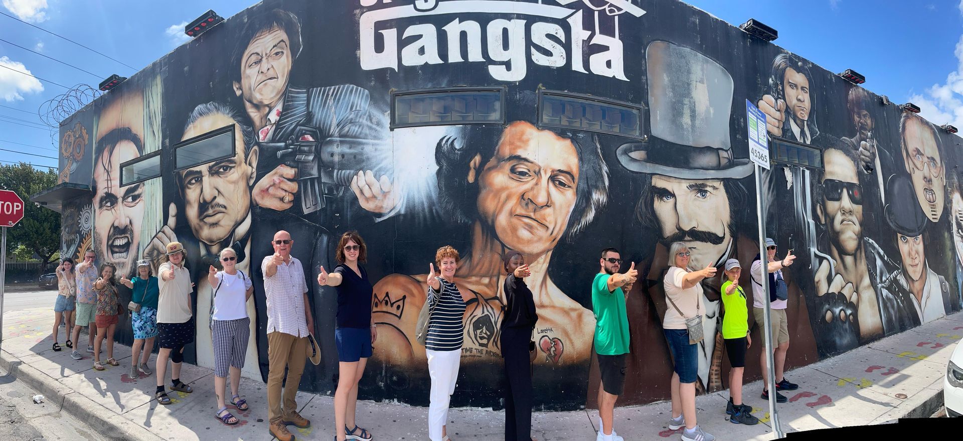 Passengers and tour guide taking photos in Wynwood Walls with the Gangster Mural behind them. 