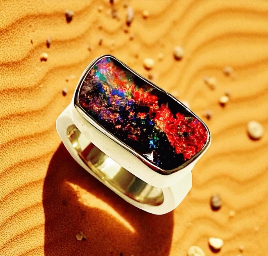 Ring With a Vibrant Black Opal Stone Set in White Metal, on Sand — Regency Jewellers in Cairns City, QLD