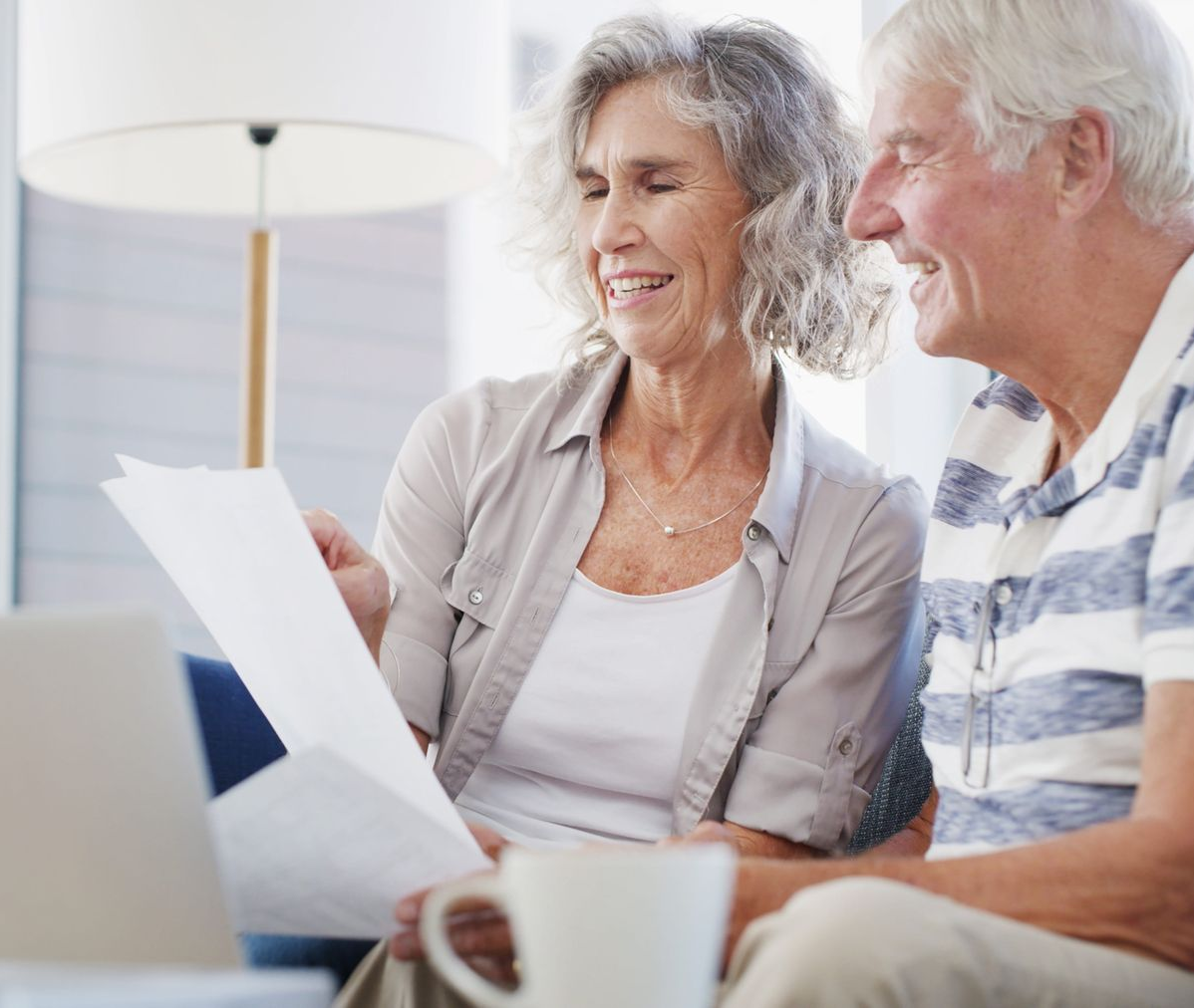 Smiling couple reviewing papers together on a couch in a bright living room