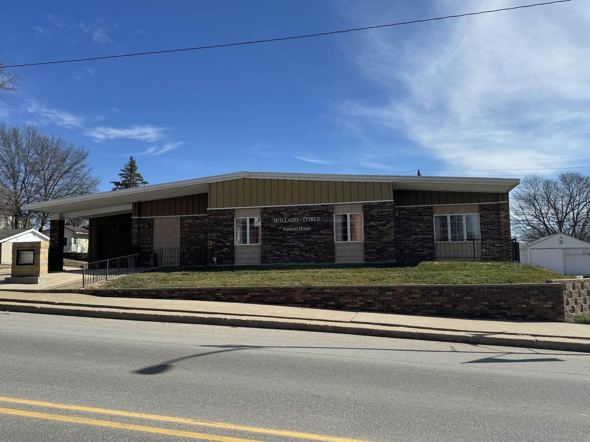 Single-story brick building with a flat roof and a small parking lot under a blue sky