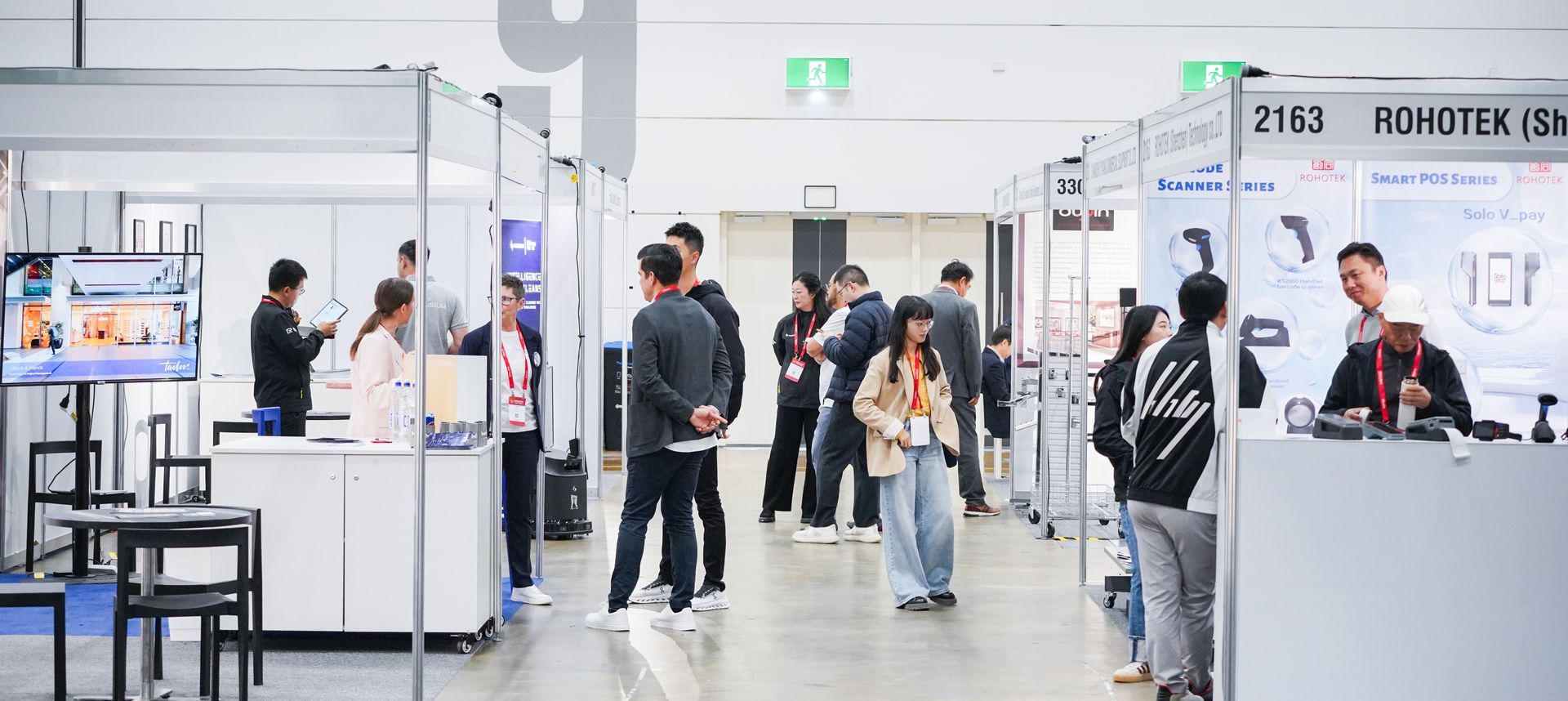Busy indoor trade show hall with booths, people walking, and exhibitors at counters
