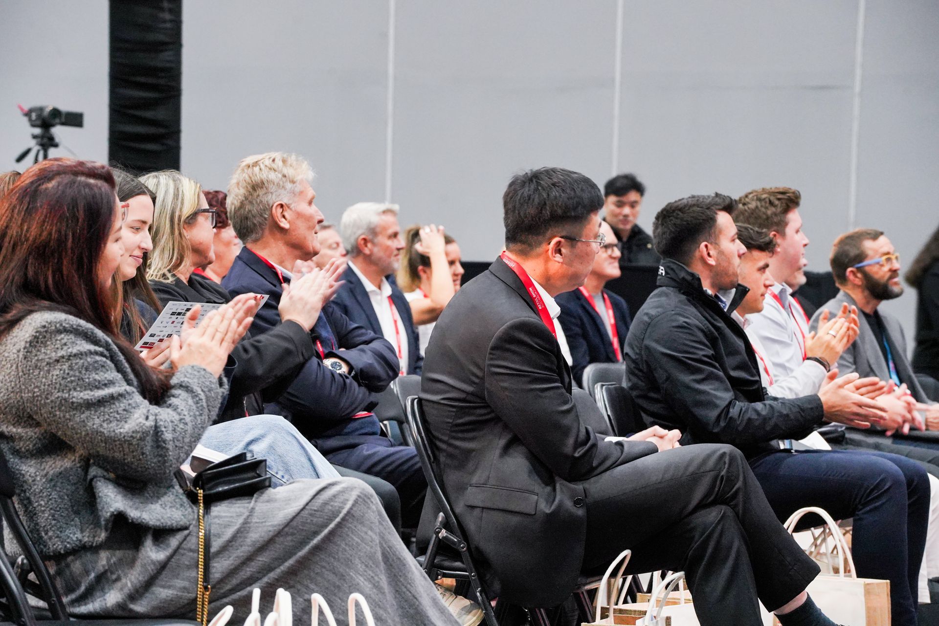Audience seated and applauding at a conference, with a woman in a gray sweater in the foreground