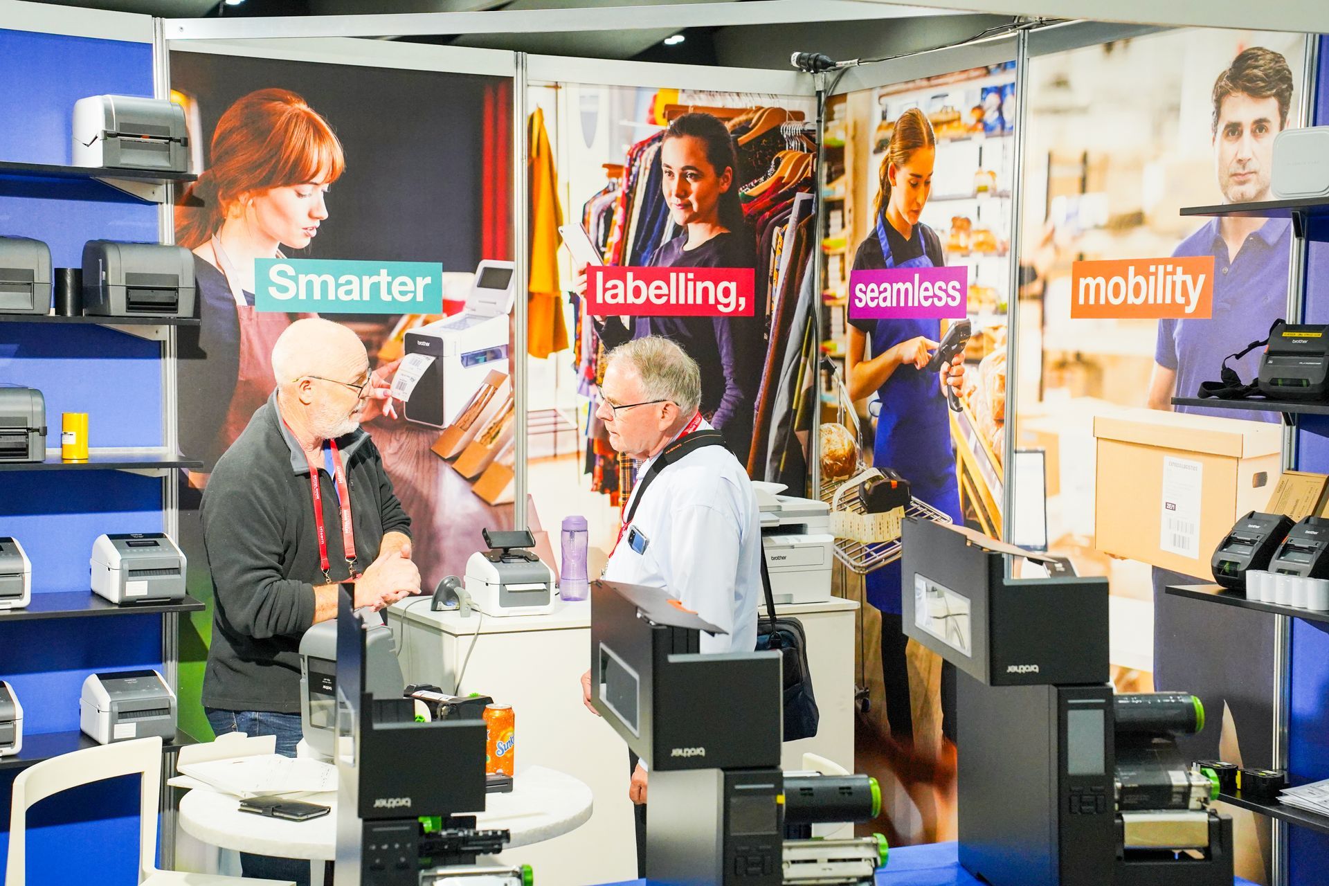 Business expo booth with people discussing technology displays and signs reading smarter, labeling, services, mobility