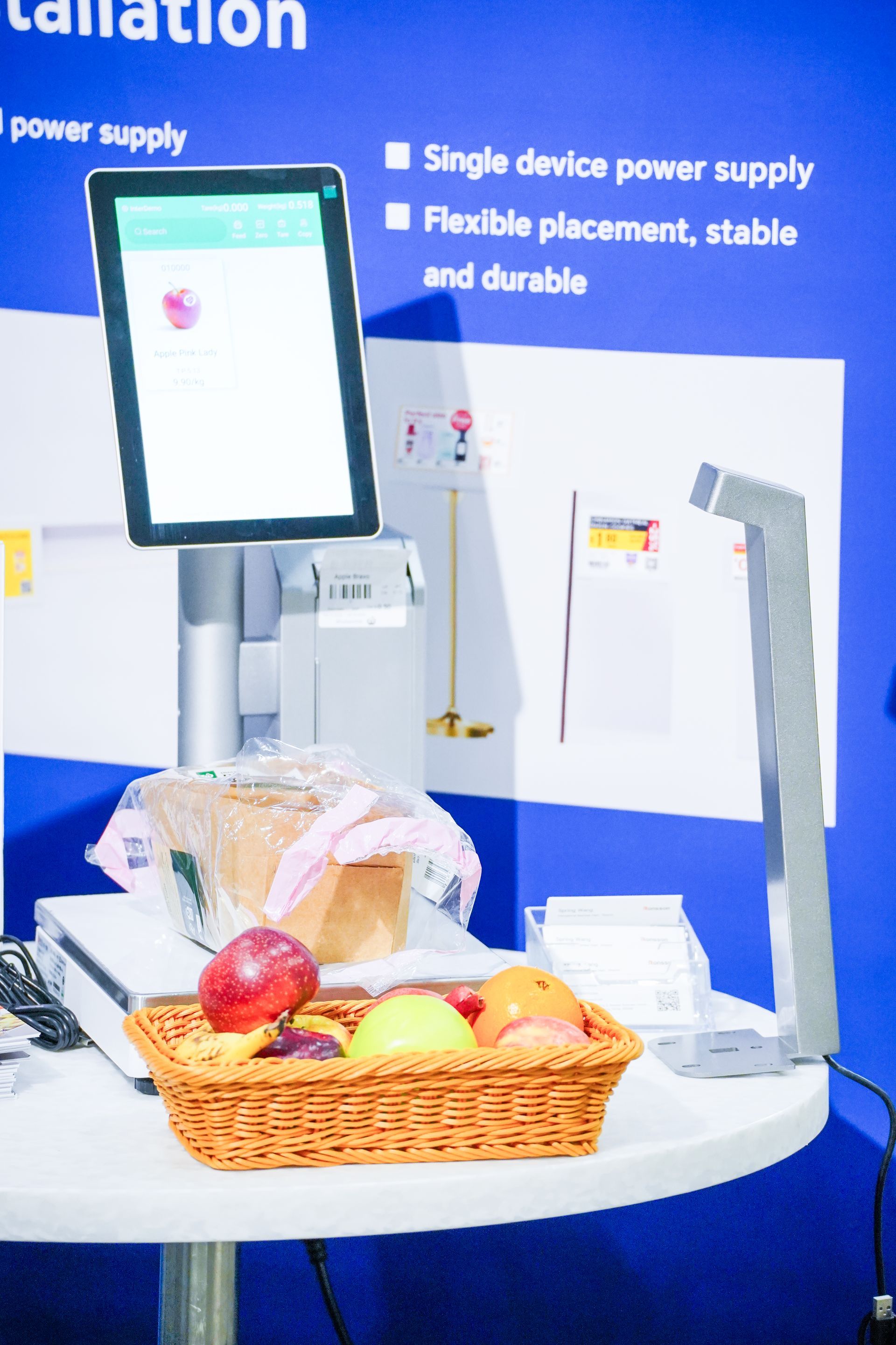 White countertop display with touchscreen device, bread, fruit basket, and dairy products against a blue background