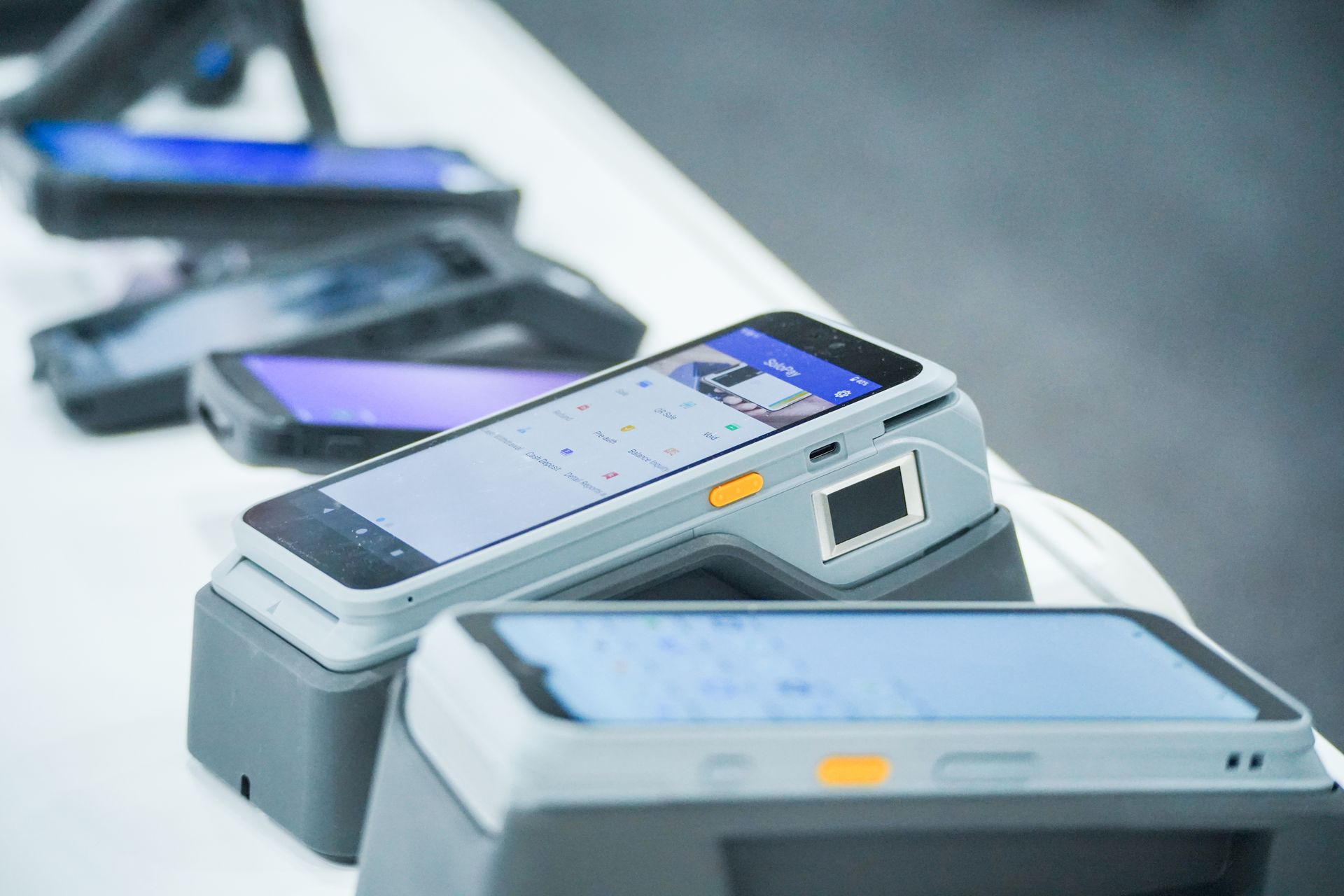 Row of silver smartphones with lit screens on a white surface, viewed in shallow focus