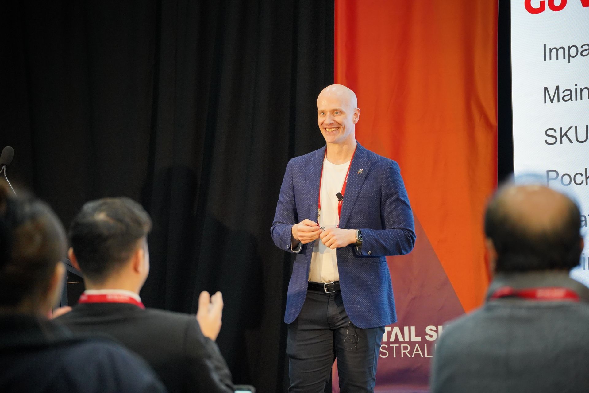 Speaker on stage in blue blazer presenting to an audience at a conference