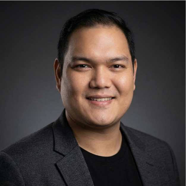 Studio headshot of a smiling person in a dark blazer against a gray background
