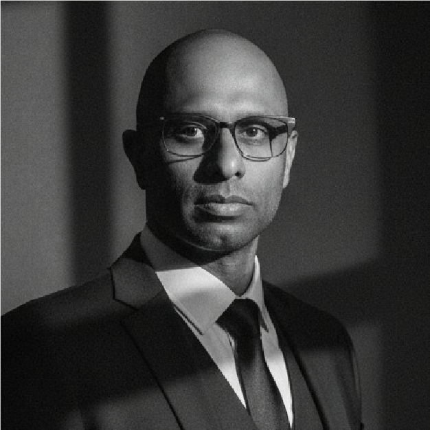 Black-and-white portrait of a man in glasses and a suit against a dark background