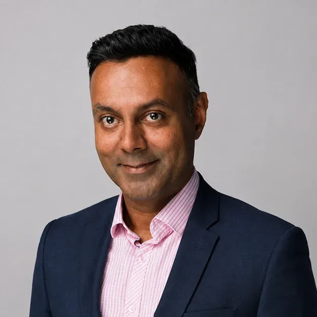 Studio headshot of a smiling person in a dark blazer against a gray background