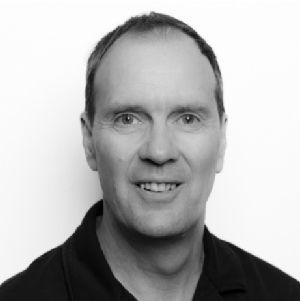 Black-and-white headshot of a smiling man in a dark collared shirt