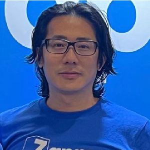 Man wearing glasses and a blue T-shirt standing against a blue background with white circular graphics