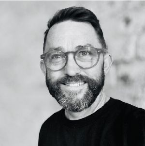 Smiling bearded man wearing glasses against a soft gray background