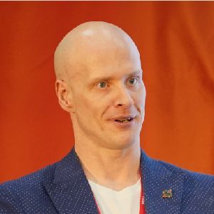 Person speaking on stage in a blue blazer against an orange background