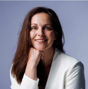 Smiling woman with long dark hair, resting her chin on her hand against a blue-gray background