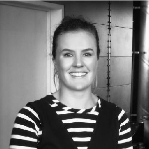Smiling person in a striped shirt standing indoors against a doorway and wall.