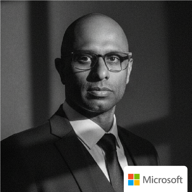 Black-and-white portrait of a man in a suit and glasses, with a Microsoft logo in the corner