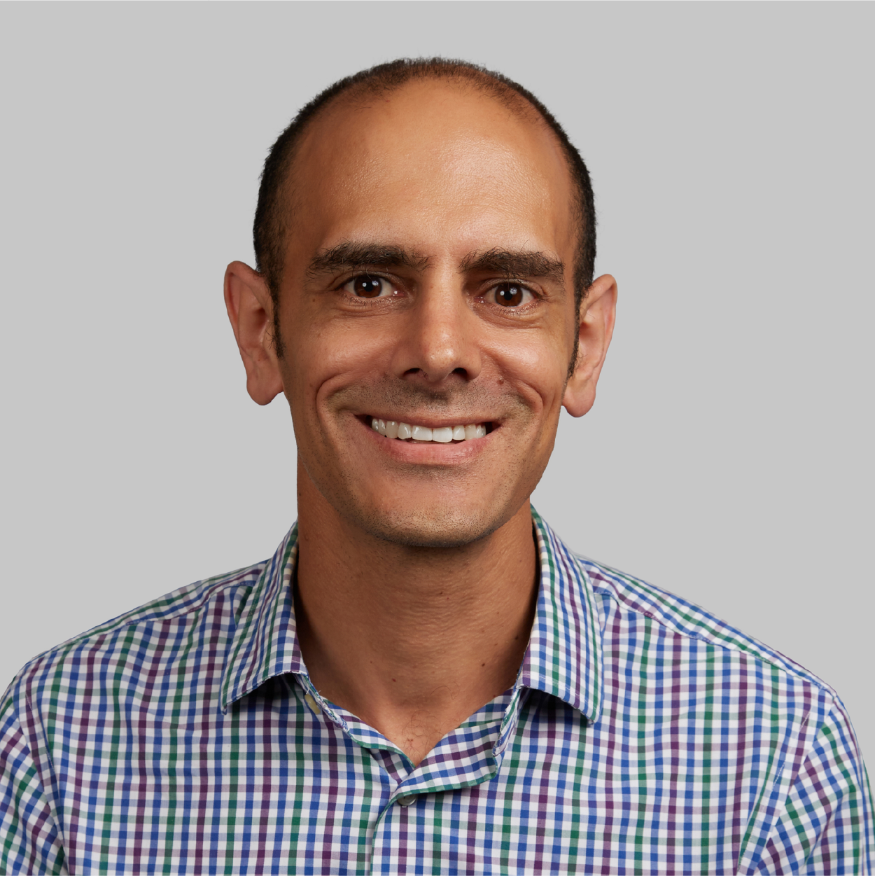 Smiling man in a blue, green, and white plaid shirt against a gray background