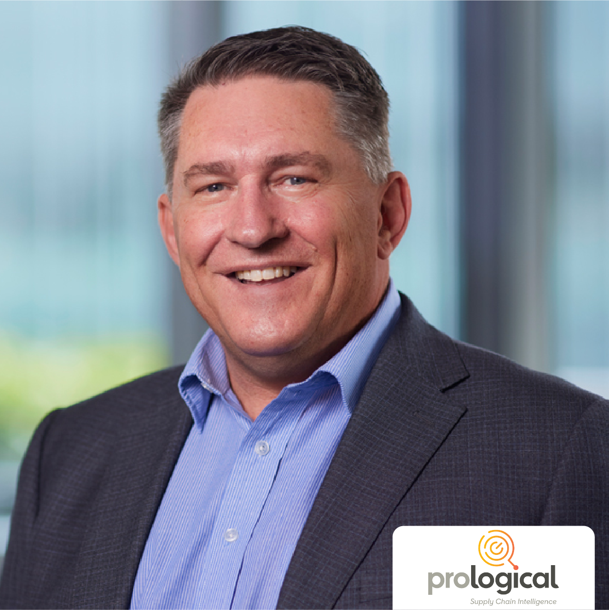Smiling man in a dark blazer and blue shirt against a blurred office background with a Prological logo.