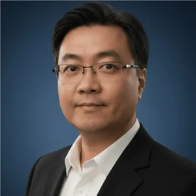 Studio portrait of a man in glasses wearing a dark suit and white shirt against a blue background