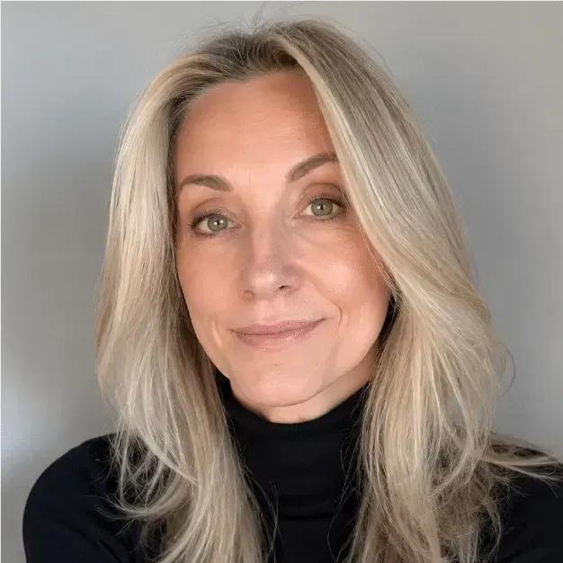 Portrait of a blonde person in a black turtleneck, facing forward with a neutral expression against a gray background