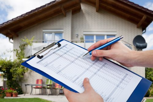 A person is writing on a clipboard in front of a house.