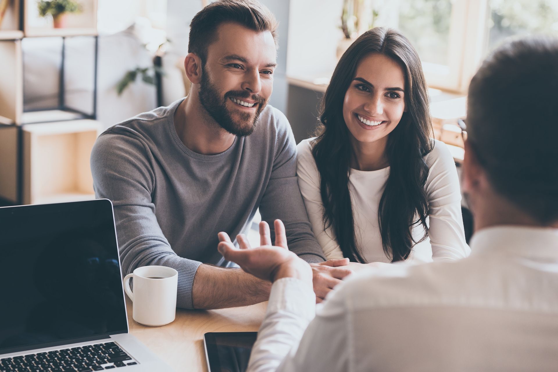 A man and a woman are sitting at a table talking to a man.