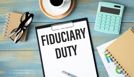Desk with a “Fiduciary Duty” document, coffee cup, calculator, glasses, and notebook.