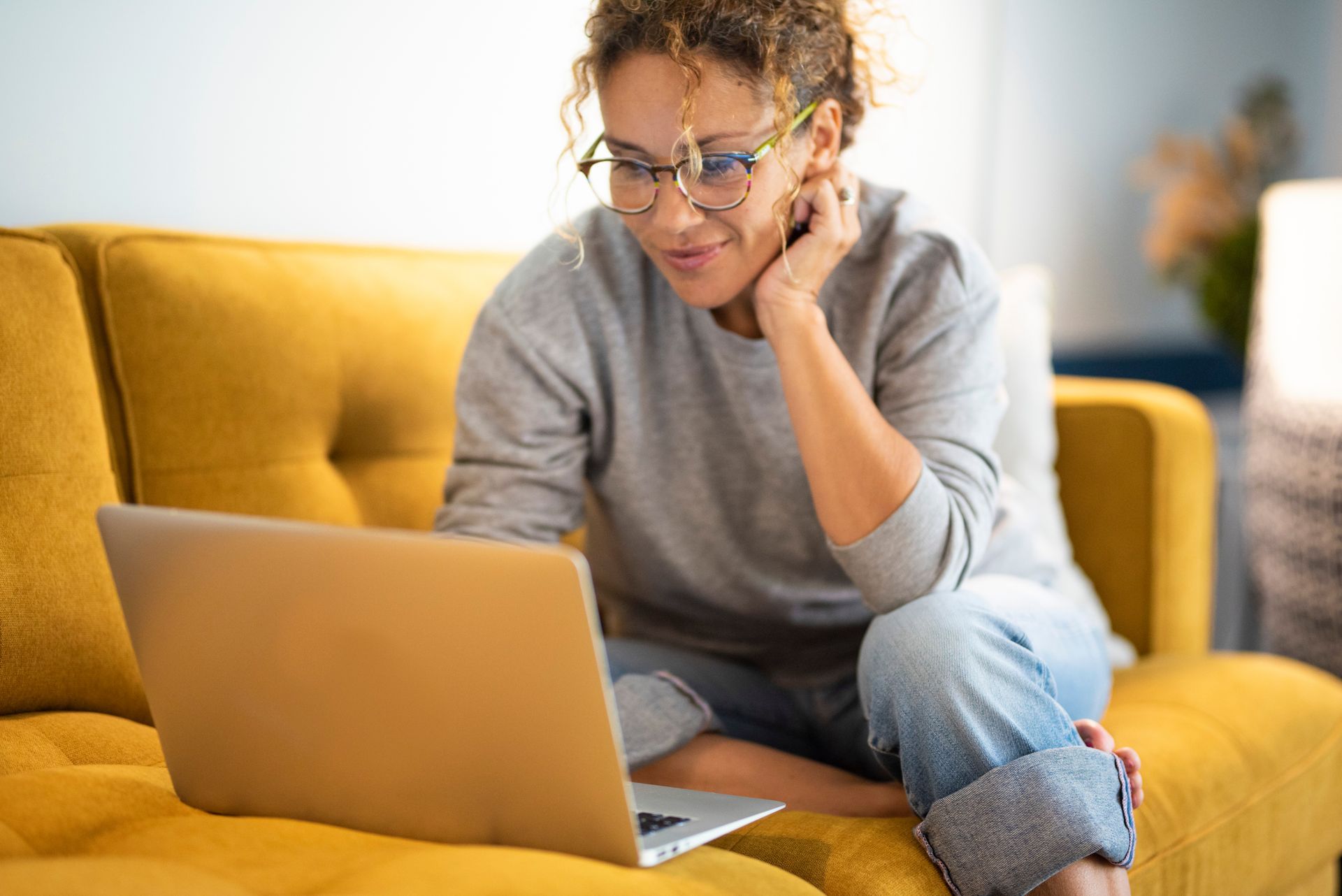 A woman is sitting on a yellow couch using a laptop computer.