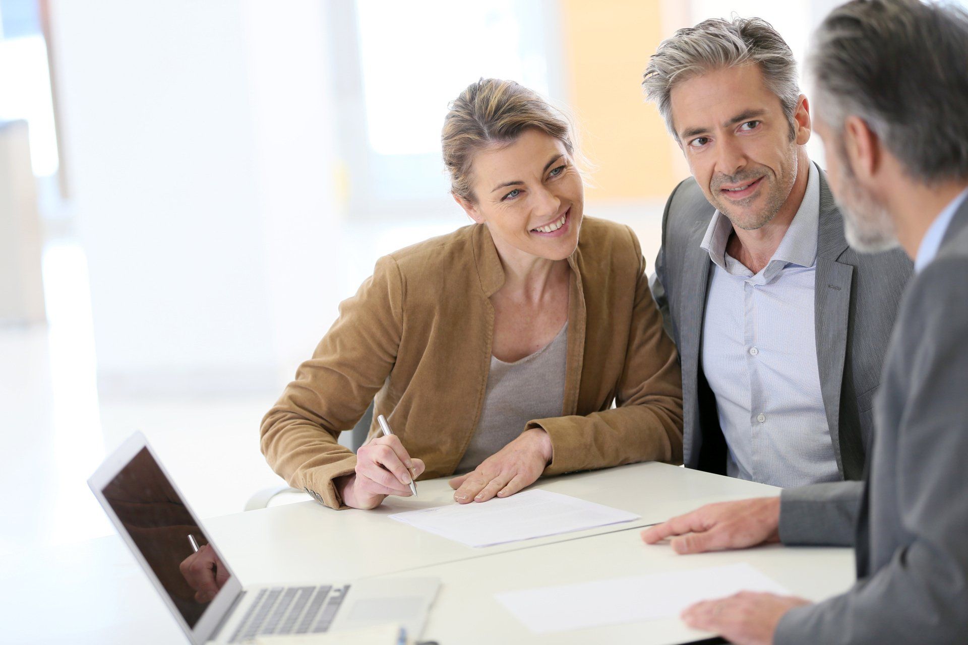Two coworkers discussing documents at a bright office table with a laptop open nearby