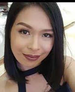 Close-up portrait of a person with shoulder-length dark hair, wearing a black choker and a slight smile.