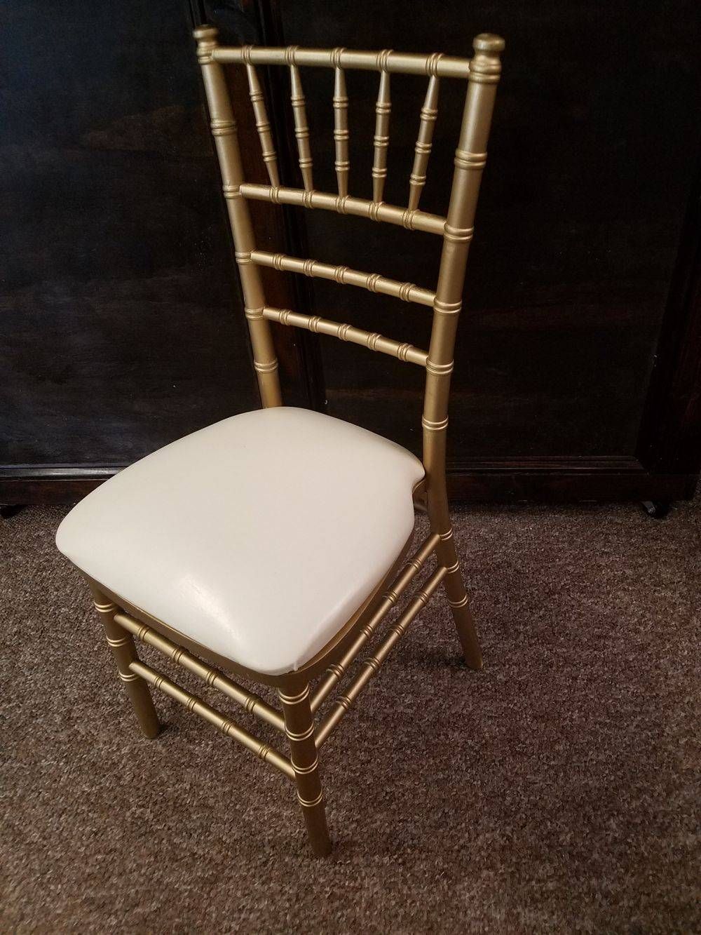 A gold chiavari chair with a white seat cushion