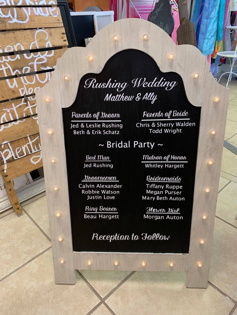 A sign for a wedding with lights on it is sitting on a tiled floor.