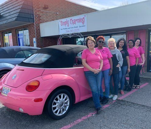 A group of women are standing in front of a pink car.
