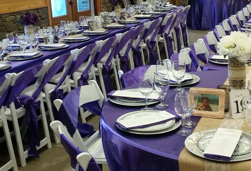 A long table set for a wedding reception with purple tables and white chairs.