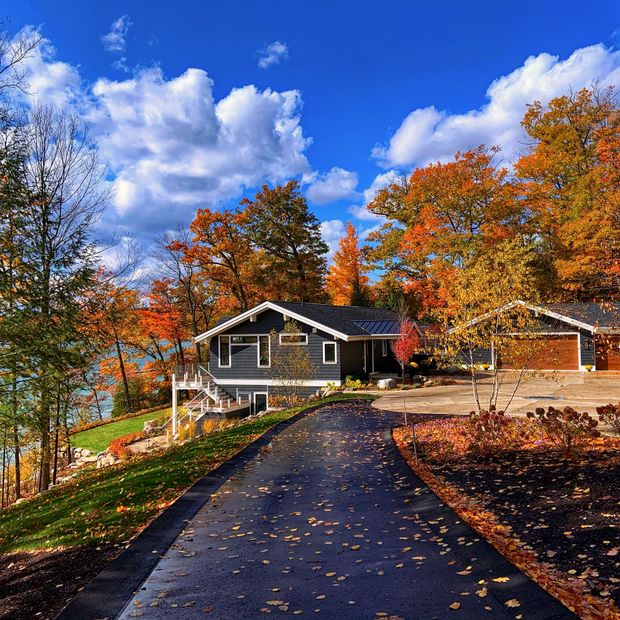 Autumn cabin with paved driveway, surrounded by colorful fall trees under a bright blue sky