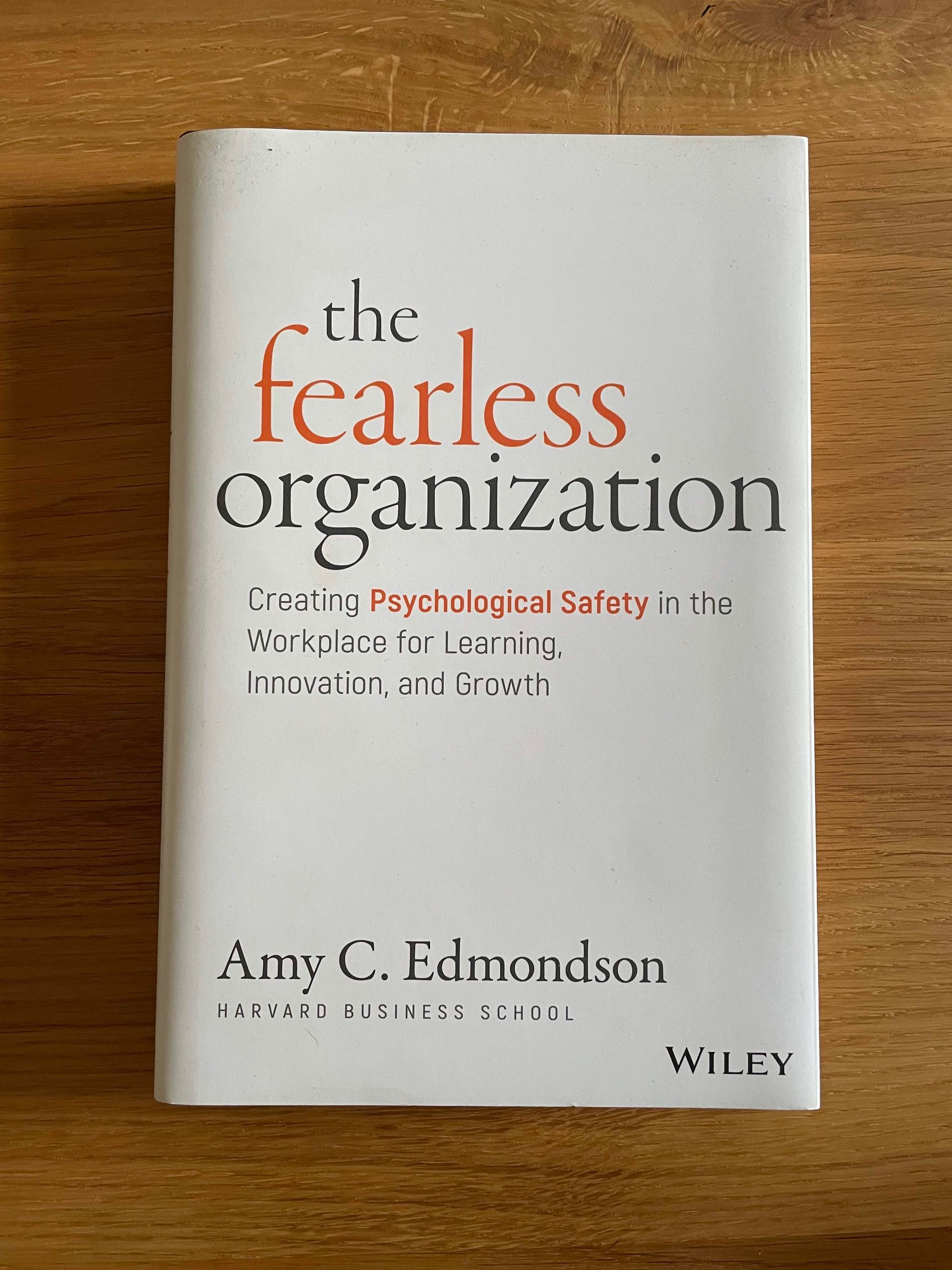 Foto des englischen Buchcovers von The Fearless Organization von Amy C. Edmondson auf einer Holzoberfläche. Das Buchcover isr weiß mit schwarzer und orangener Schrift. Der Untertitel lautet: creating psychological safety in the workplace for learning, innovation, and growth.