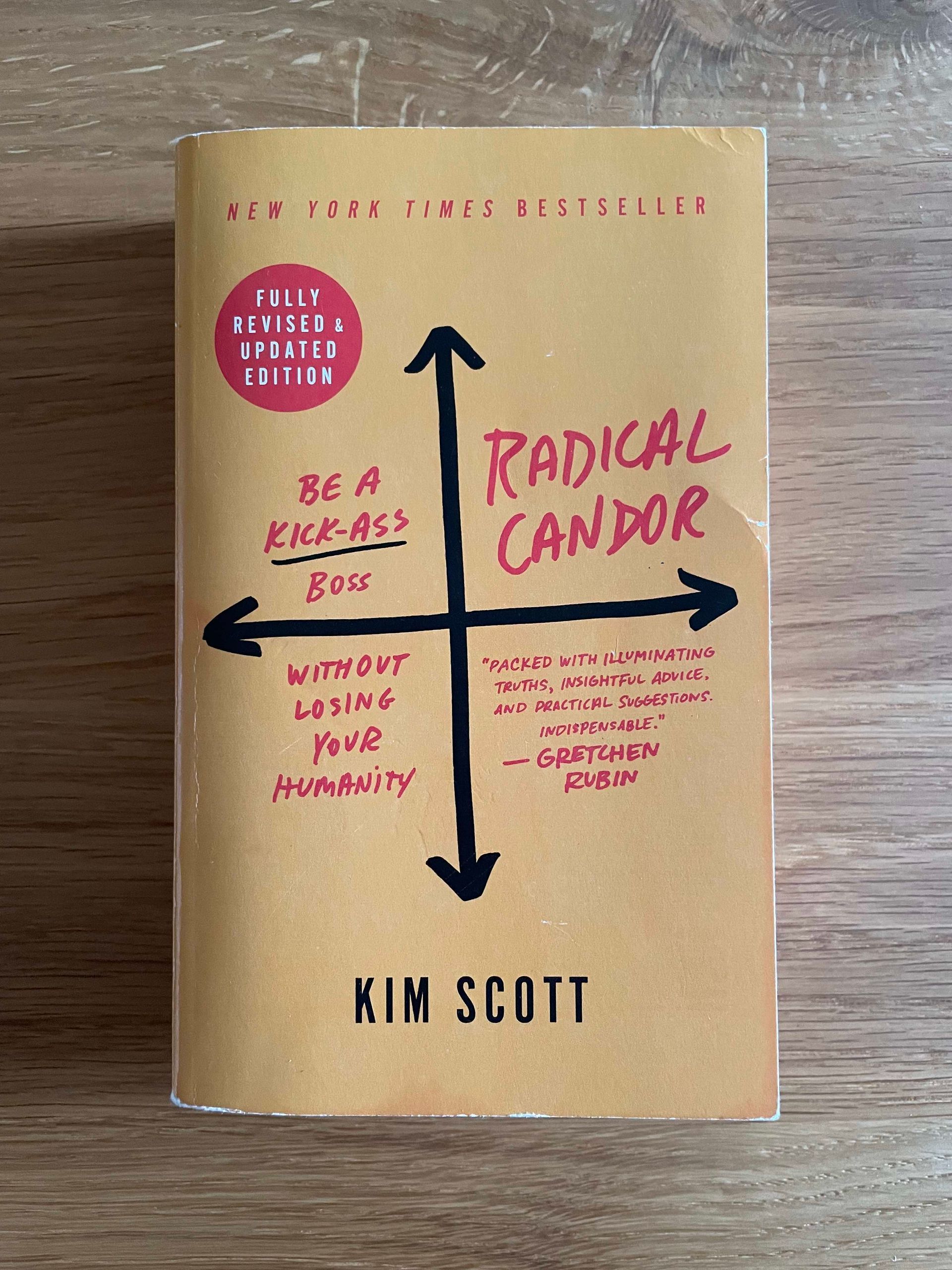 Foto des englischen Buchcovers von Radical Candor von Kim Scott auf einer Holzoberfläche. Das Buchcover ist gelb mit schwarzer und roter Schrift. Der Untertitel lautet: be a kick-ass boss without losing your humanity.