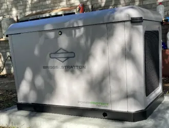 A generator is sitting outside of a brick building.