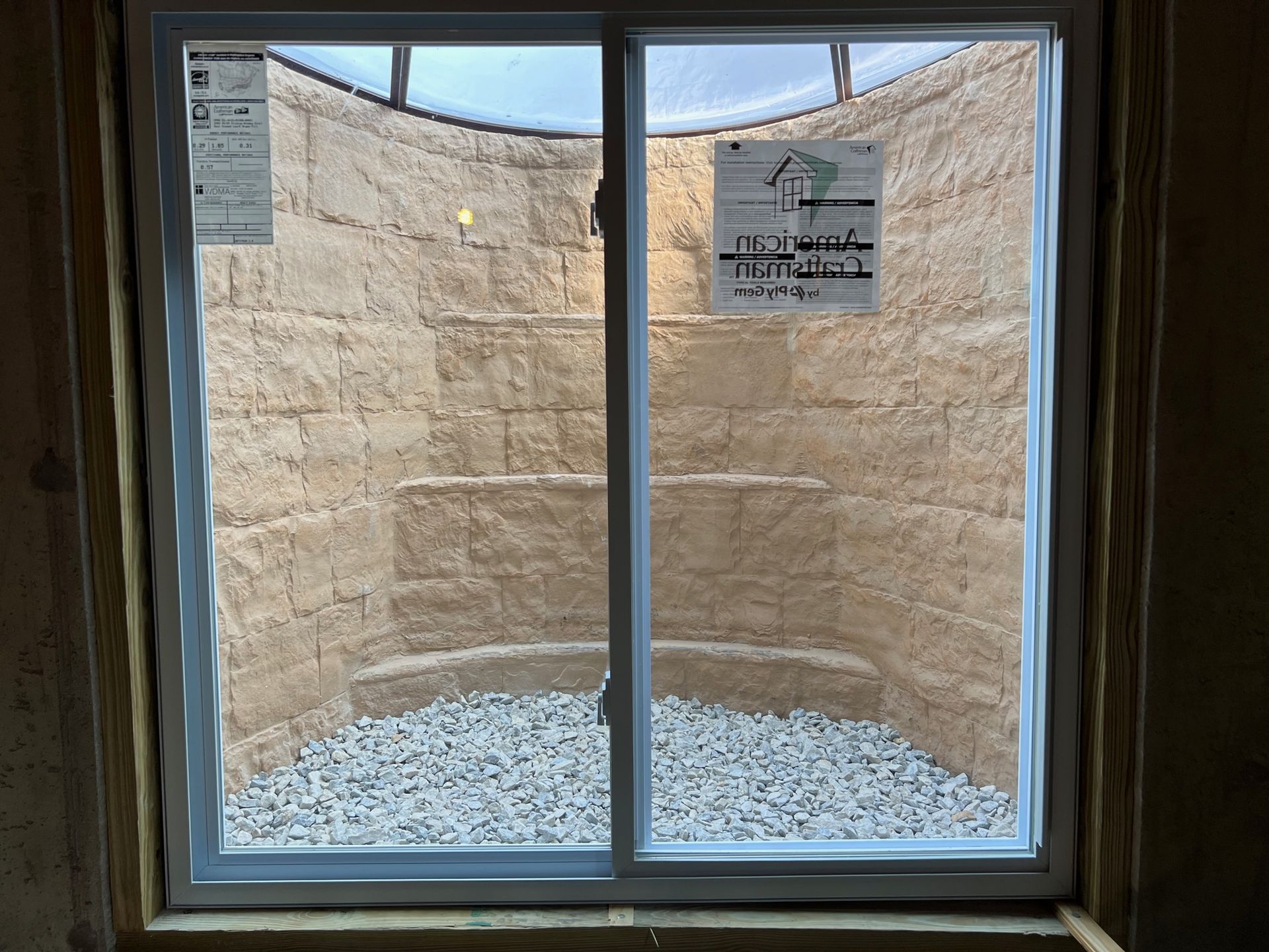 View through a window into a small stone courtyard with gravel and signs on the far wall.