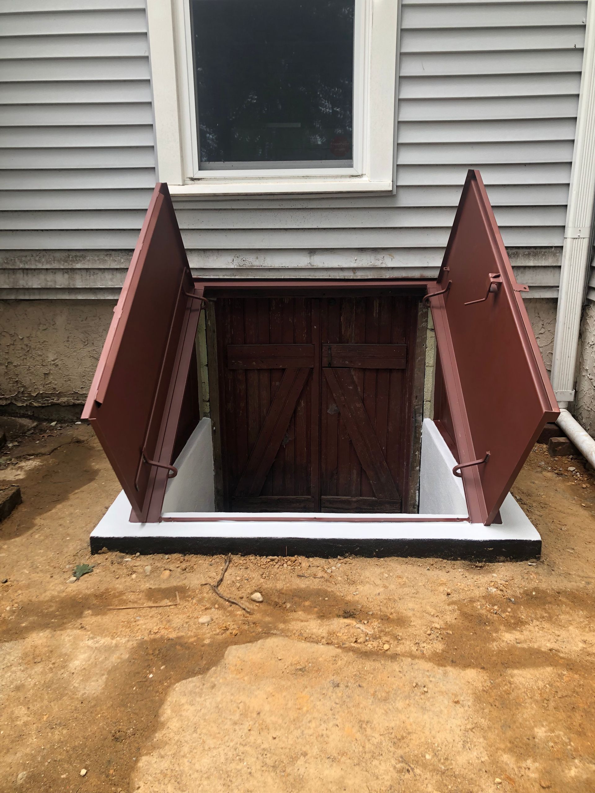 Basement stairwell with open red metal doors and a white concrete frame beside a house foundation
