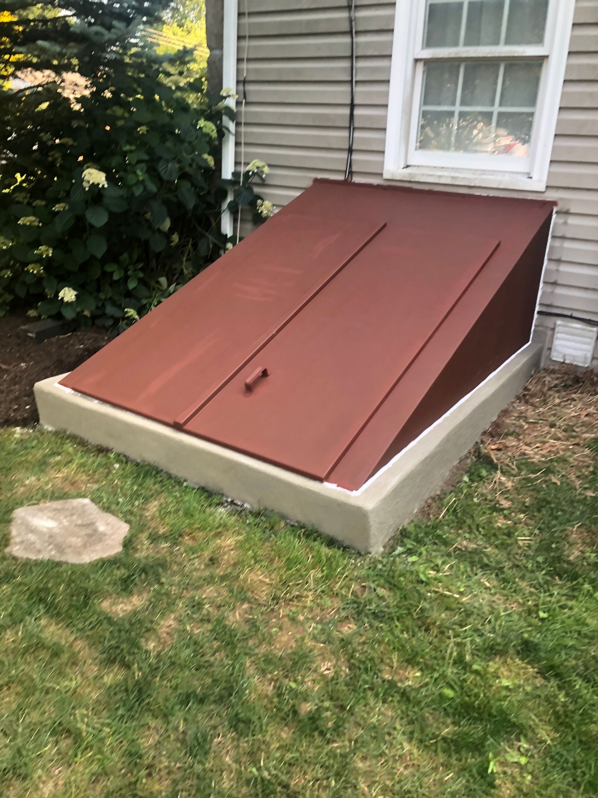 Basement stairwell covered by a red sloped door beside a house foundation