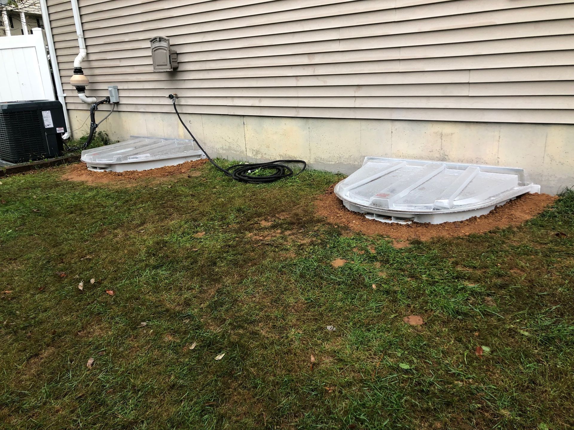 Backyard basement window wells beside beige house siding and grass lawn