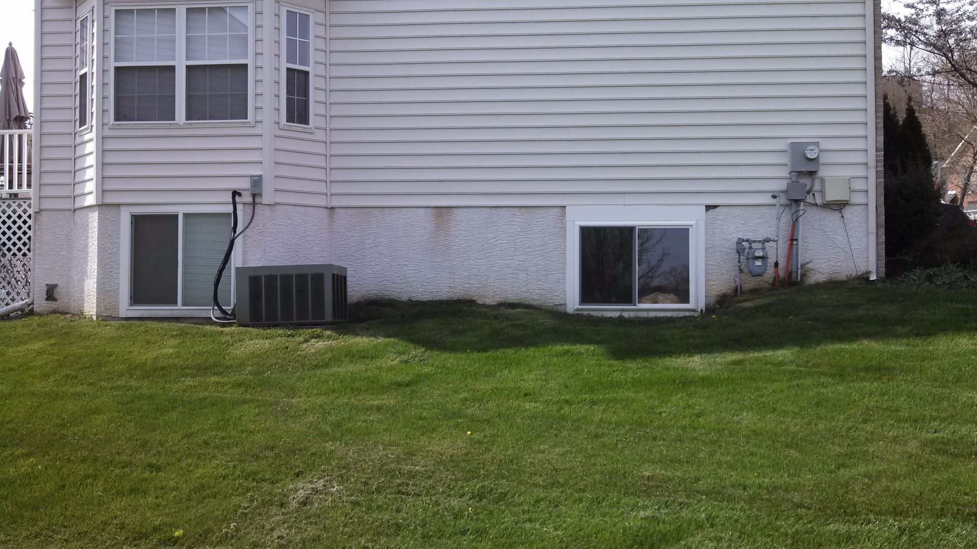 Backyard of a beige house with small basement windows and a green lawn.