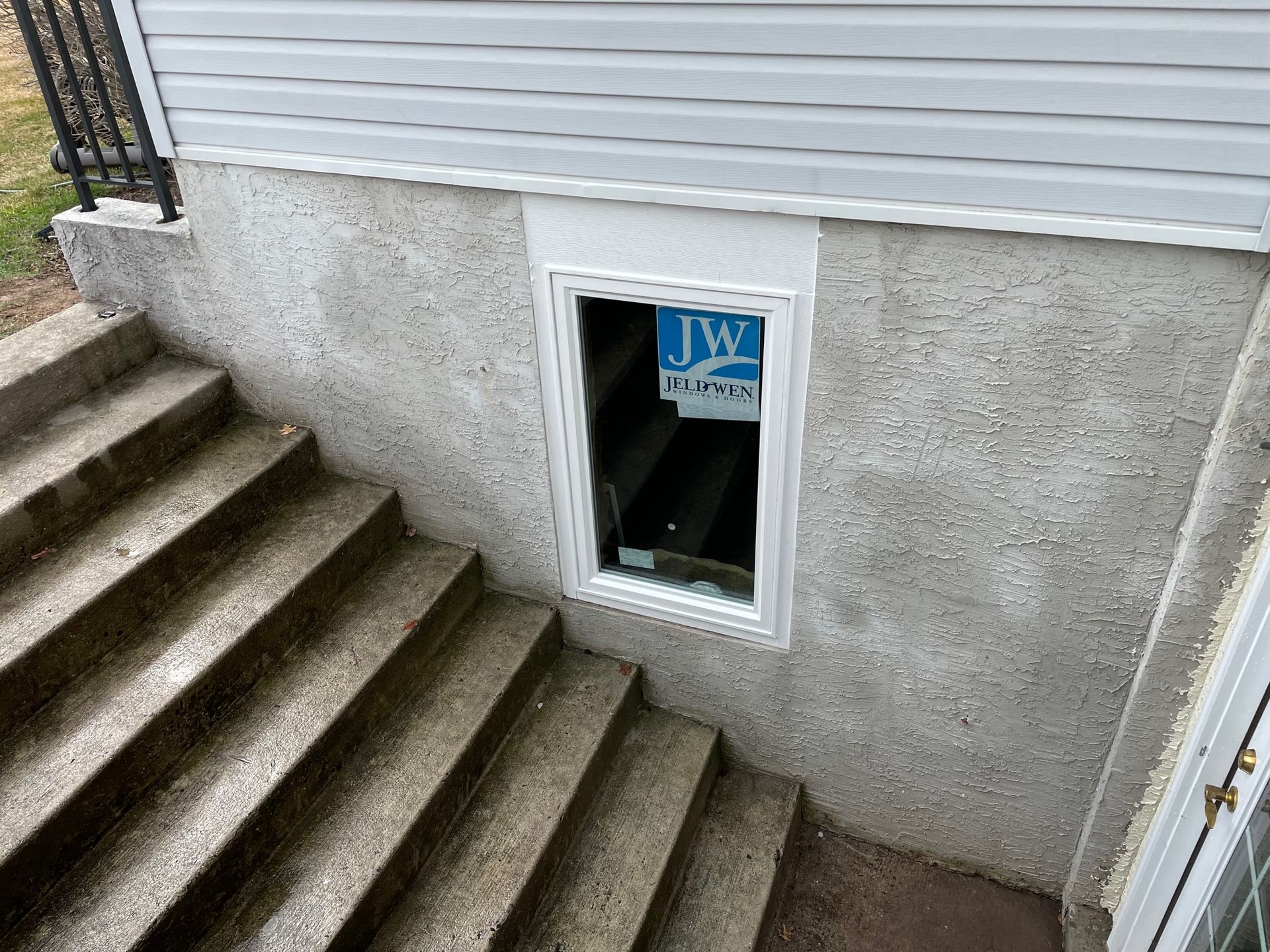 A window in the basement of a house with stairs leading up to it.