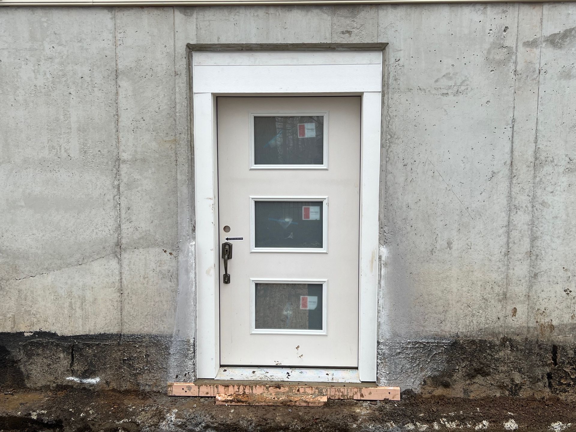 A white door is sitting in the dirt next to a house.